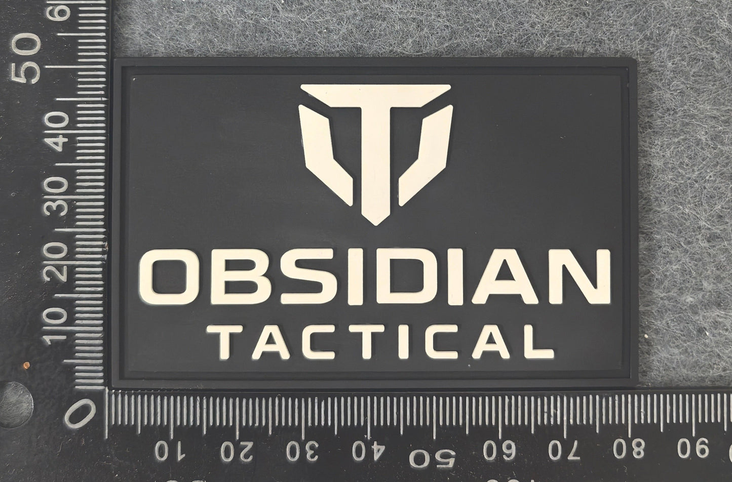 Obsidian Tactical logo patch on a textured surface with a ruler for scale.