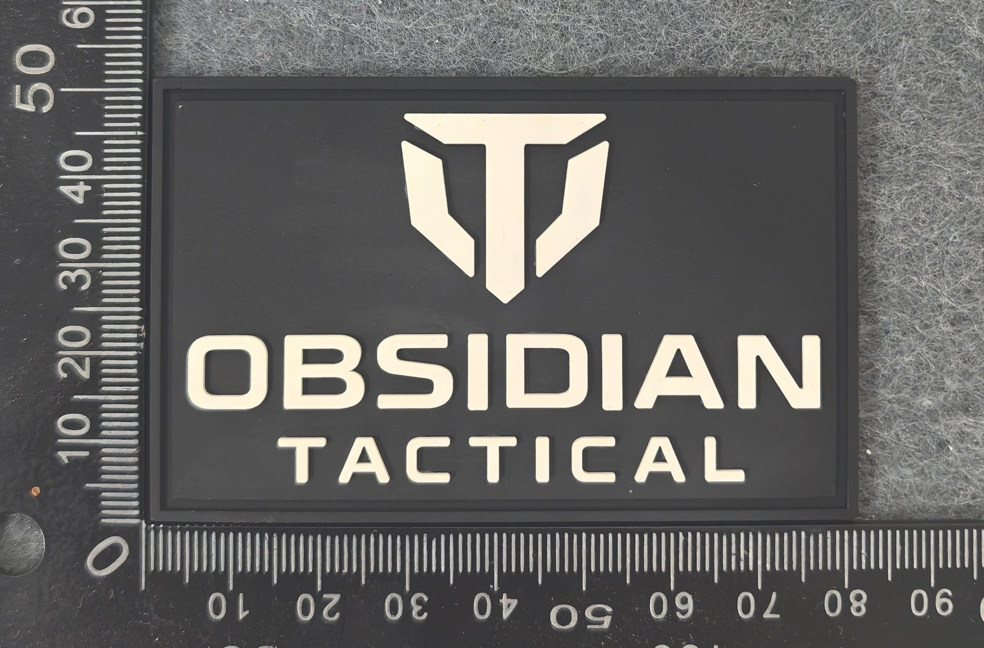 Obsidian Tactical logo patch on a textured surface with a ruler for scale.